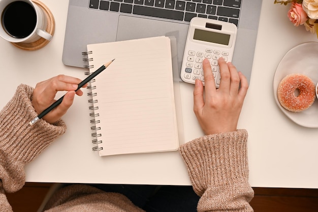 Vue aérienne d'une femme utilisant une calculatrice pour calculer son revenu et ses dépenses mensuels