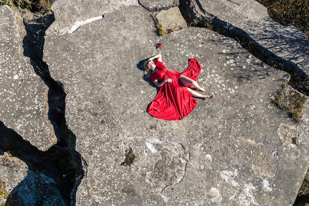 Vue aérienne sur une fille en robe rouge allongée sur une structure en ruine rocheuse ou en béton