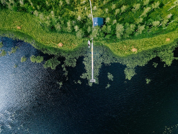 Vue aérienne de la forêt et du lac bleu avec reflet des nuages en Finlande Maison de sauna au bord du lac Jetée en bois avec bateaux de pêche