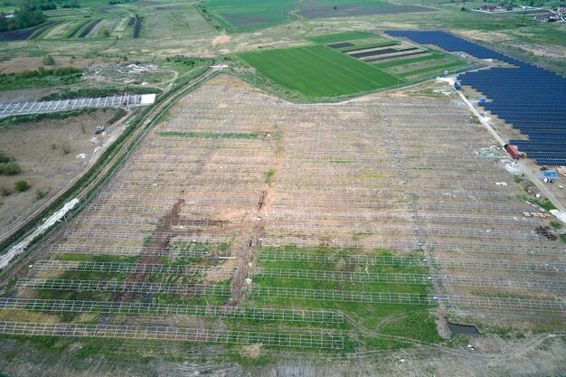 Vue aérienne d'une grande centrale électrique en construction avec de nombreuses rangées de panneaux solaires sur châssis métallique pour produire de l'énergie électrique propre Développement de sources d'électricité renouvelables