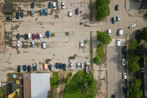 Vue aérienne de haut en bas de la rue animée avec circulation de voitures en mouvement et grand parking avec de nombreux véhicules garés.