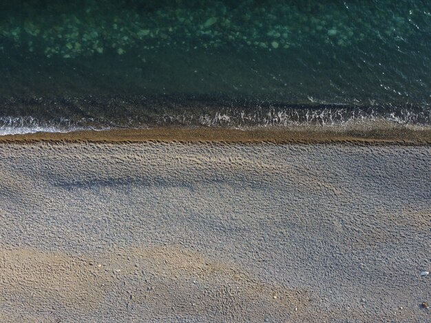 Vue aérienne d'en haut sur la mer d'azur et la plage de galets de petites vagues sur une surface d'eau cristalline en