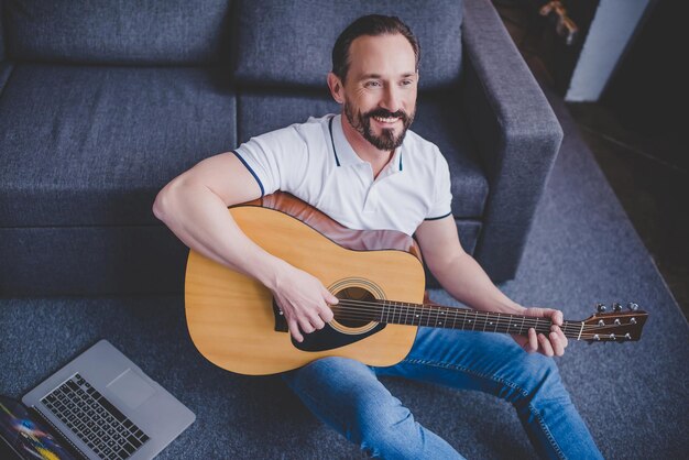 Vue aérienne d'un homme jouant de la guitare assis sur le sol à la maison