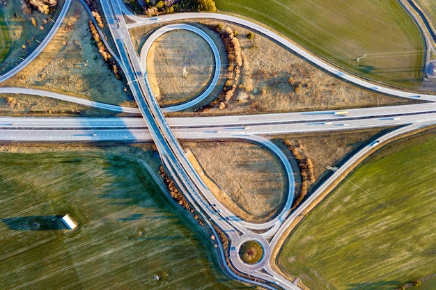 Vue aérienne de l'intersection de la route moderne, toits de maison sur le champ vert de printemps