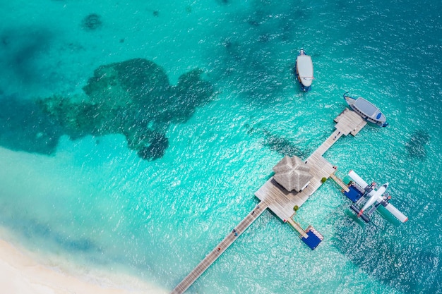 Vue aérienne de la jetée du bungalow sur l'eau et du fond bleu de la mer aux Maldives. Hydravion et bateaux en bois