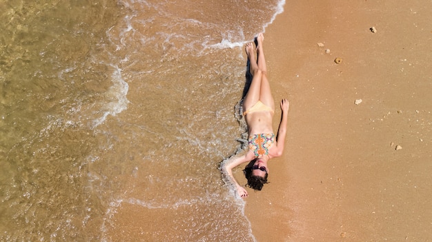 Vue aérienne de jeune femme en bikini se détendre sur la plage tropicale de sable par la mer et les vagues d'en haut, fille sur les vacances à la plage de l'île tropicale en Thaïlande