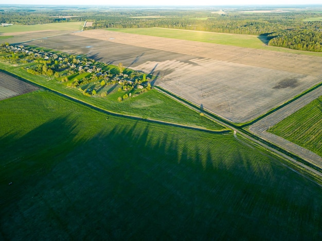 Vue aérienne d'un magnifique champ agricole le long de la forêt au coucher du soleil Vue du haut des champs criblés de routes de terre rurales Paysage naturel