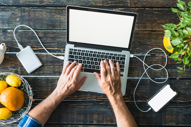 Vue Aérienne De La Main De L'homme En Tapant Sur Un Ordinateur Portable Connecté Avec Banque D'alimentation Et Téléphone Portable