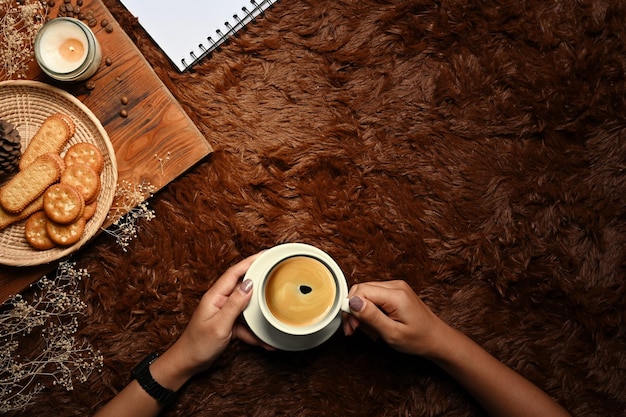 Vue aérienne mains de femme tenant une tasse de café chaud sur un tapis marron