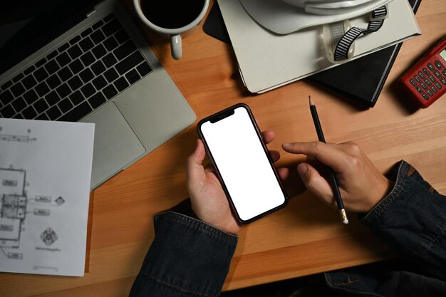 Vue aérienne des mains d'un ingénieur tenant un téléphone intelligent sur son poste de travail Écran vide pour votre publicité