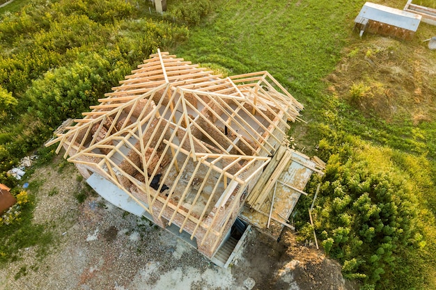 Vue aérienne d'une maison en brique inachevée avec une structure de toit en bois en construction.