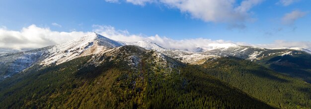 Vue aérienne de montagnes majestueuses couvertes de forêt d'épinettes vertes et de hauts sommets enneigés.