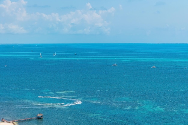 Vue aérienne d'un navire nautique ou de yachts naviguant sur une belle surface d'eau de mer bleue contre un ciel nuageux avec une jetée sur la côte