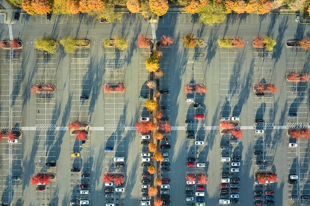 Photo vue aérienne de nombreuses voitures colorées stationnées sur un parking avec des lignes et des marquages pour les places de stationnement et les directions place pour les véhicules devant une place d'un centre commercial