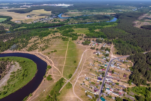 Vue aérienne panoramique de l'éco-village avec des maisons en bois, des routes de gravier, des jardins et des vergers.