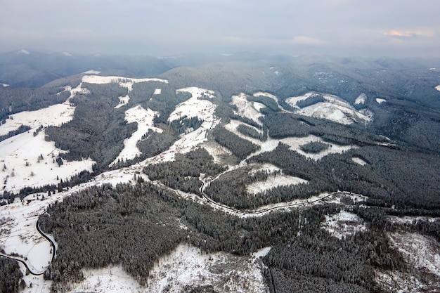 Vue aérienne d'un paysage d'hiver aride avec des collines montagneuses couvertes d'une forêt de pins à feuilles persistantes après de fortes chutes de neige par une soirée froide et calme.
