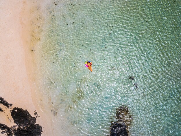 Vue aérienne de personnes en vacances d'été avec une belle fille sur un lilo tendance coloré se détendre et bronzer sur l'eau de plage du lagon océan vert clair