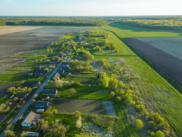 Vue aérienne d'un petit village près d'une route de terre De grands champs multicolores plantés de diverses cultures agricoles Champ de blé vue d'oiseau