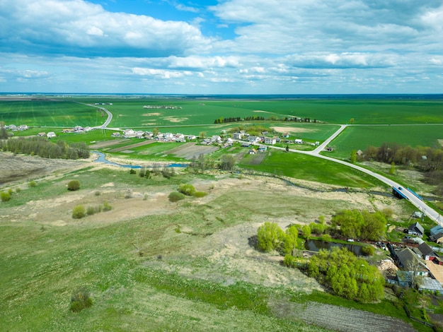 Vue aérienne d'un petit village près d'une route de terre De grands champs multicolores plantés de diverses cultures agricoles Champ de blé vue d'oiseau