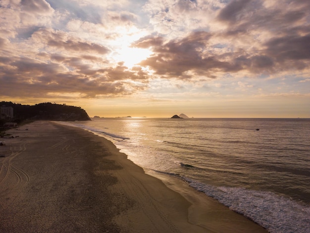 Vue aérienne de la plage de Barra da Tijuca, un paradis à l'ouest de Rio de Janeiro, au Brésil. De grandes collines autour comme Pedra da GÃ¡vea. Journée ensoleillée avec quelques nuages à l'aube. Mer verdâtre. Photo drone.