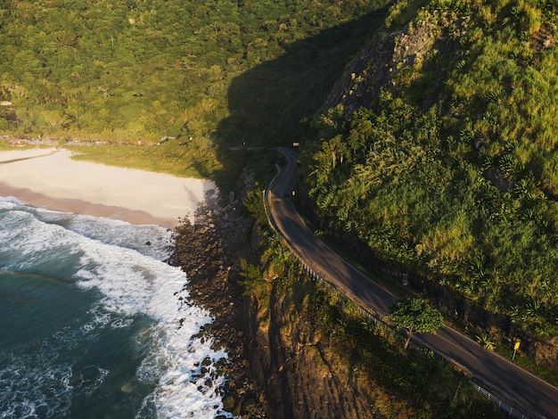 Vue aérienne de la plage de Prainha, un paradis à l'ouest de Rio de Janeiro, au Brésil. Grandes collines autour. Journée ensoleillée à l'aube. Mer verdâtre. Photo drone.