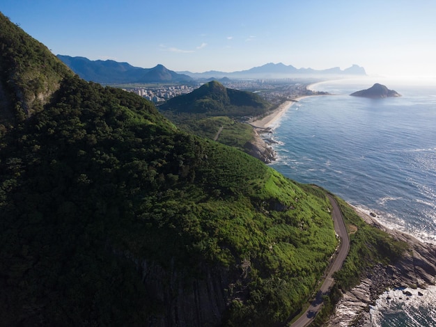 Vue aérienne de la plage de Prainha, un paradis à Rio de Janeiro, Brésil. Grandes collines autour. En arrière-plan, les plages de Recreio dos Bandeirantes. Journée ensoleillée à l'aube. Mer verdâtre. Photo drone.