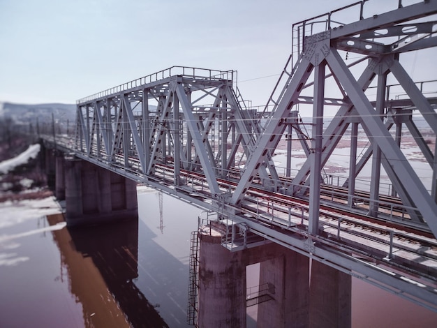 Vue aérienne d'un pont ferroviaire sur un lac de tourbe avec de l'eau brun clair et des restes de glace