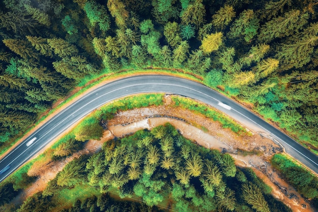 Vue aérienne de la route dans la belle forêt verte au coucher du soleil en automne Paysage coloré avec des pins de la chaussée voitures floues et rivière dans les montagnes des Carpates Vue de dessus de l'autoroute Voyage en Ukraine