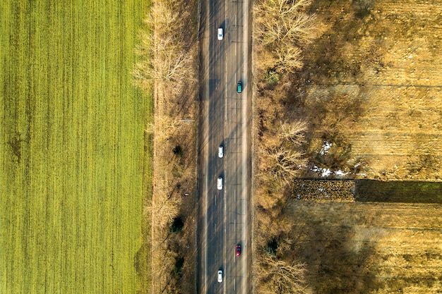 Vue aérienne de la route droite avec des voitures en mouvement, des arbres et des champs verts aux beaux jours. Photographie de drone.