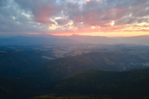 Vue aérienne d'une soirée brumeuse sur un pic élevé avec des pins sombres au coucher du soleil. Paysage incroyable de bois de montagne sauvage au crépuscule