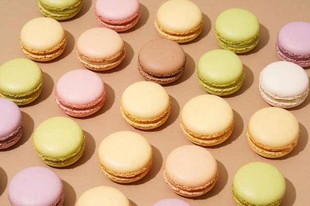 Une vue aérienne d'une surface de table beige avec une gamme de macarons colorés en rangées soignées