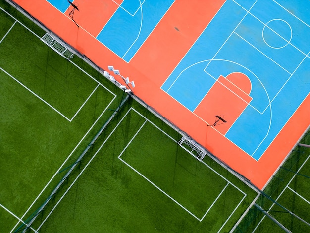 Vue aérienne d'un terrain de football vert et d'un terrain de basket coloré offrant un aperçu de deux installations sportives différentes côte à côte