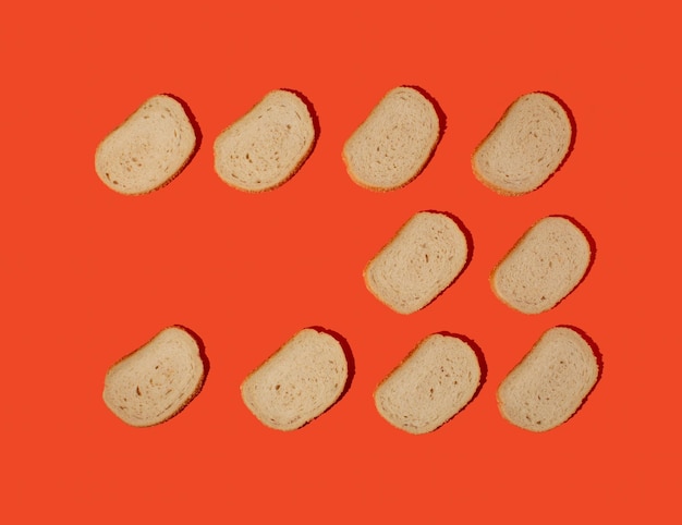 Vue aérienne de tranches de pain blanc frais disposées avec des graines de sésame sur un fond orange.
