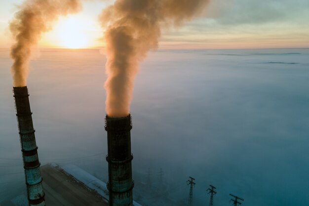 Vue aérienne des tuyaux hauts de la centrale au charbon avec de la fumée noire remontant l'atmosphère polluante au coucher du soleil.