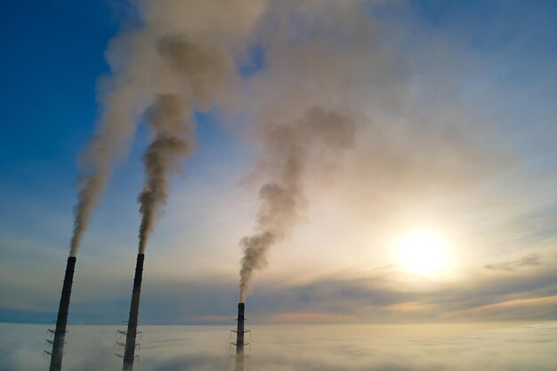 Vue aérienne des tuyaux hauts de la centrale au charbon avec de la fumée noire remontant l'atmosphère polluante au coucher du soleil