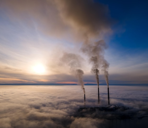 Vue aérienne des tuyaux hauts de la centrale au charbon avec de la fumée noire remontant l'atmosphère polluante au coucher du soleil.