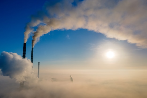 Vue aérienne des tuyaux hauts de la centrale au charbon avec de la fumée noire remontant l'atmosphère polluante au lever du soleil.