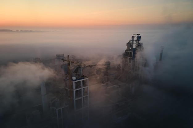 Vue aérienne de l'usine de ciment avec structure de centrale à béton élevée et grue à tour sur le site de fabrication industrielle le soir brumeux Production et concept industriel mondial