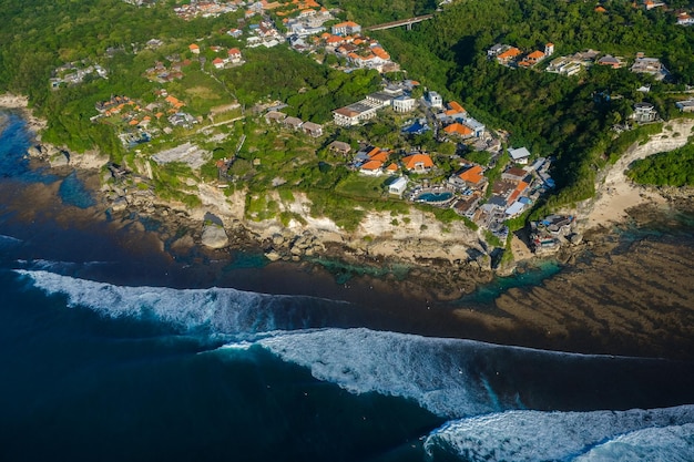 Vue aérienne d'une ville côtière avec une verdure luxuriante et des vagues qui s'écrasent sur la côte rocheuse