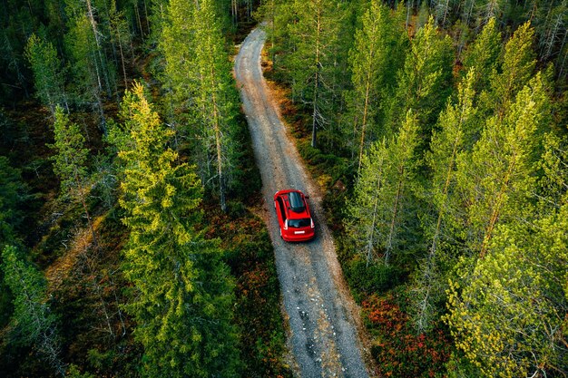 Vue aérienne d'une voiture rouge pour voyager avec une galerie de toit sur une route de campagne en Finlande