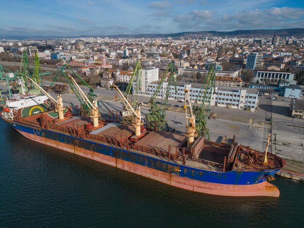 Photo vue aérienne d'un vraquier chargé de céréales est amarré dans un port animé avec des travailleurs et des machines vus en arrière-plan