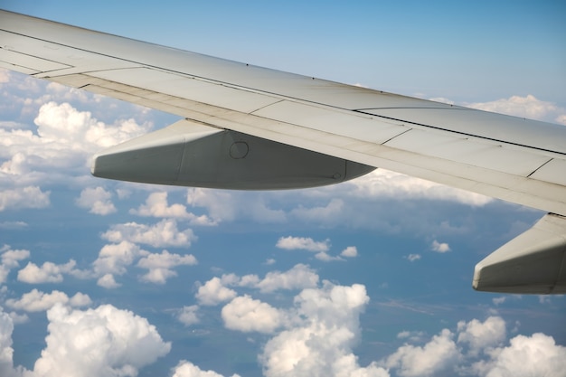 vue de l'aile d'avion à réaction de l'intérieur survolant des nuages gonflés blancs dans le ciel bleu.