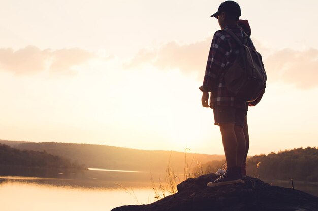 Photo vue à angle bas d'amis debout sur une roche près du lac contre le ciel au coucher du soleil