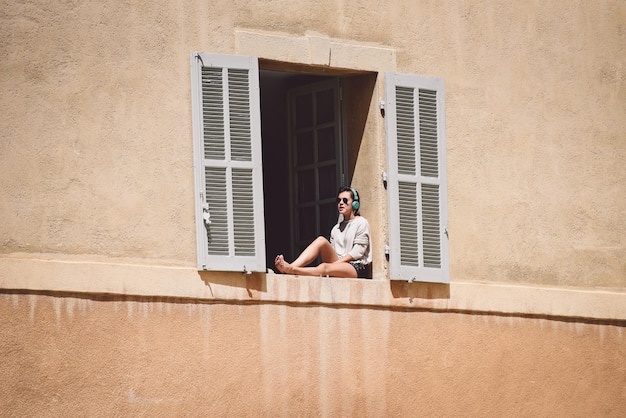 Vue à angle bas d'une femme écoutant de la musique assise sur une fenêtre