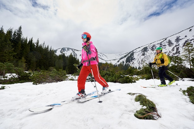 Vue à angle bas de la femme marchant sur le ski devant l'homme lors d'une excursion à ski hors piste sur les arbres du ciel de montagne en arrière-plan