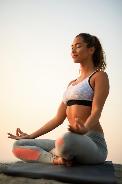 Vue en angle bas d'une femme méditant les yeux fermés tout en faisant du yoga sur un rocher contre le ciel. Copiez l'espace.