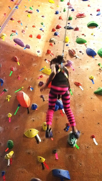 Photo vue à angle bas d'une fille grimpant sur le mur au gymnase