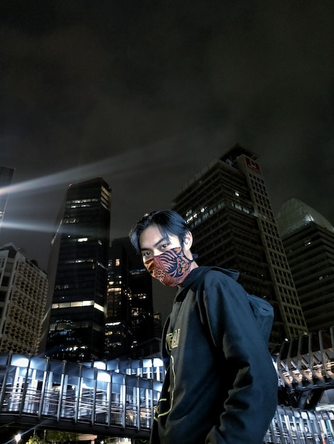 Photo vue d'angle bas de l'homme debout à des bâtiments modernes éclairés dans la ville la nuit