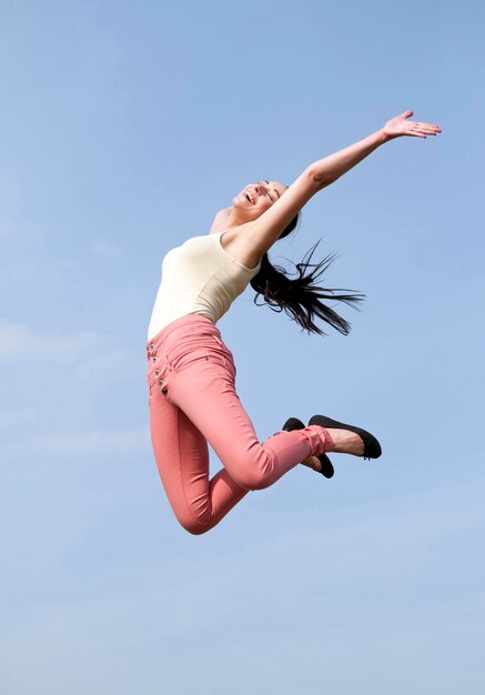 Vue à angle bas d'une jeune femme sautant contre le ciel