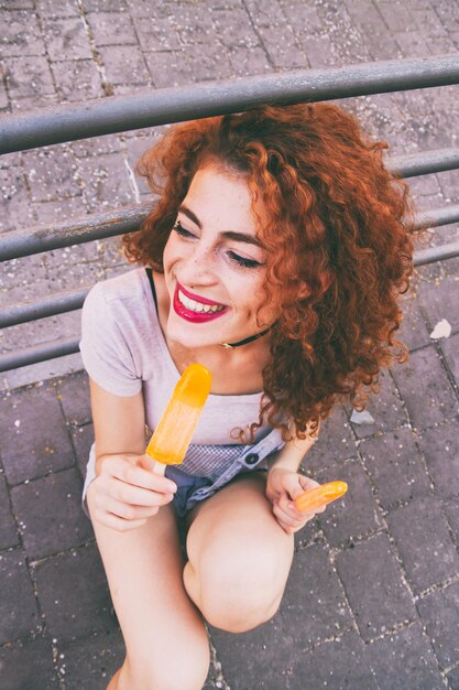 Vue d'angle élevé d'une femme heureuse ayant des glaçons orange sur le trottoir